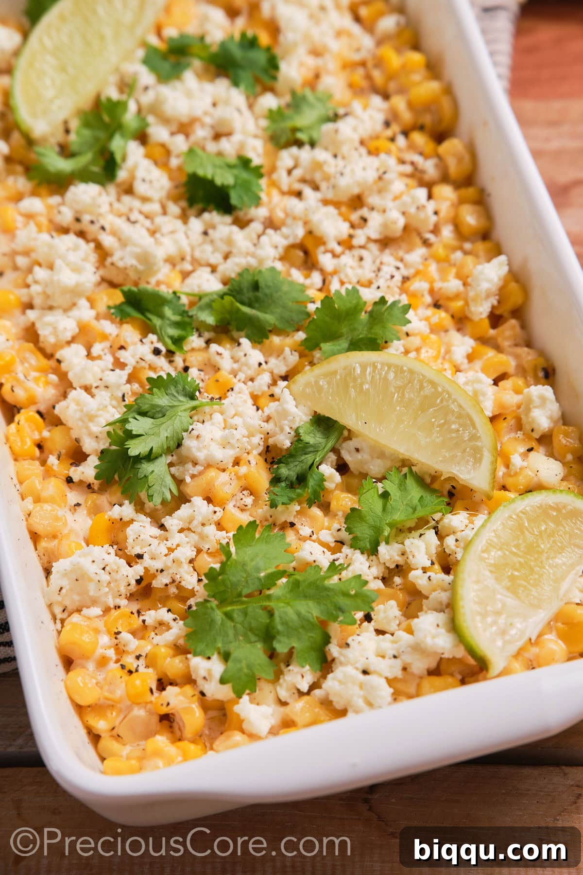 Close-up detail of the baked street corn casserole, featuring lime wedges and fresh cilantro.