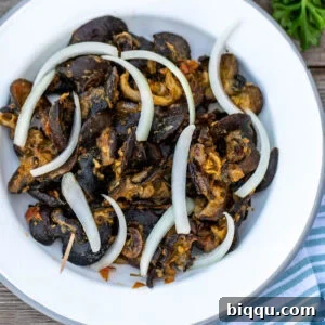 Cameroonian snails on a white plate topped with sliced onions, ready to serve.