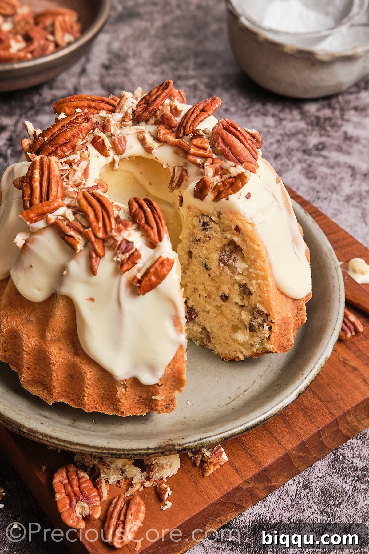 A beautifully frosted Butter Pecan Pound Cake with a slice removed, revealing its moist interior and embedded pecans.