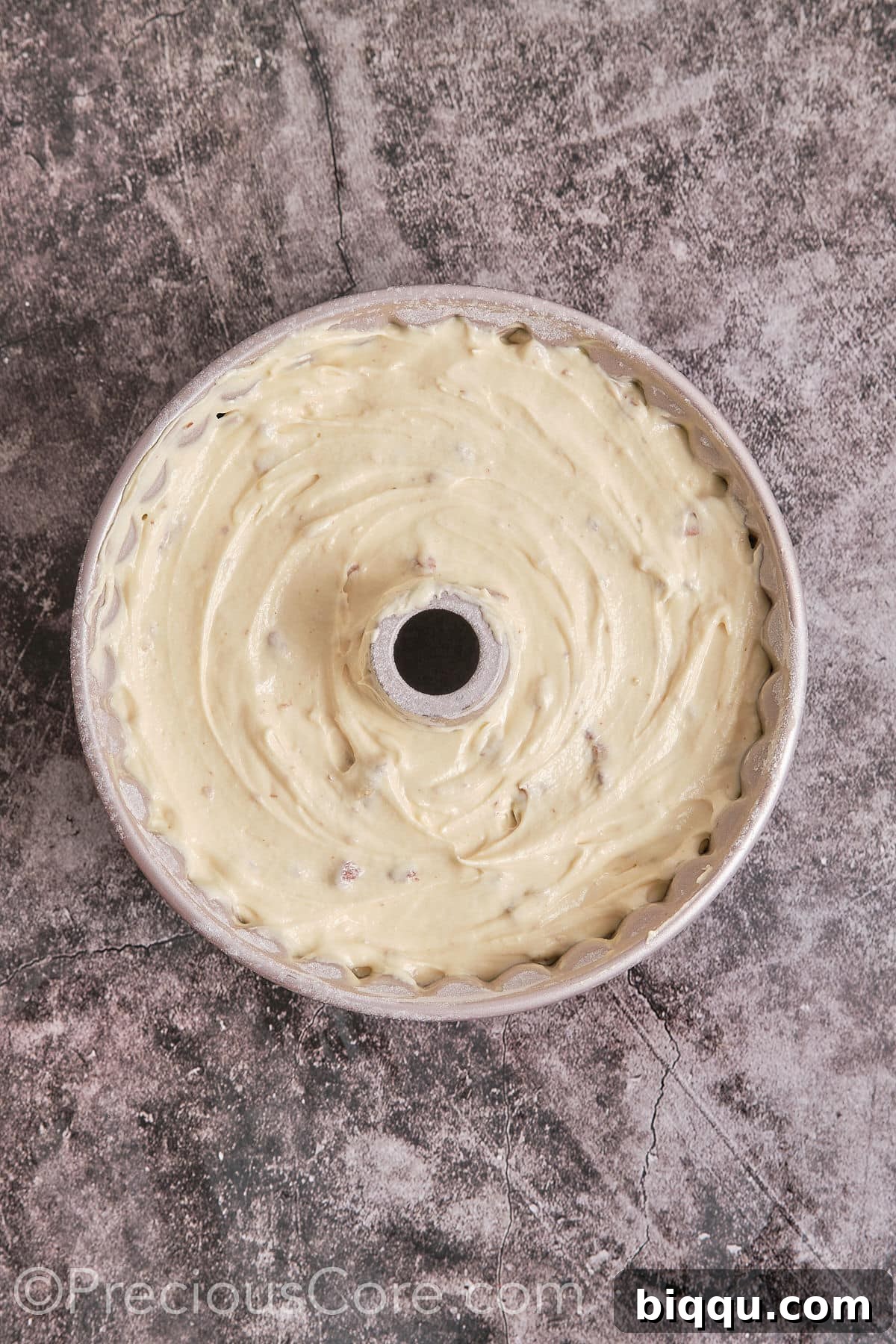 The smooth cake batter with pecans being poured into a well-greased Bundt pan.