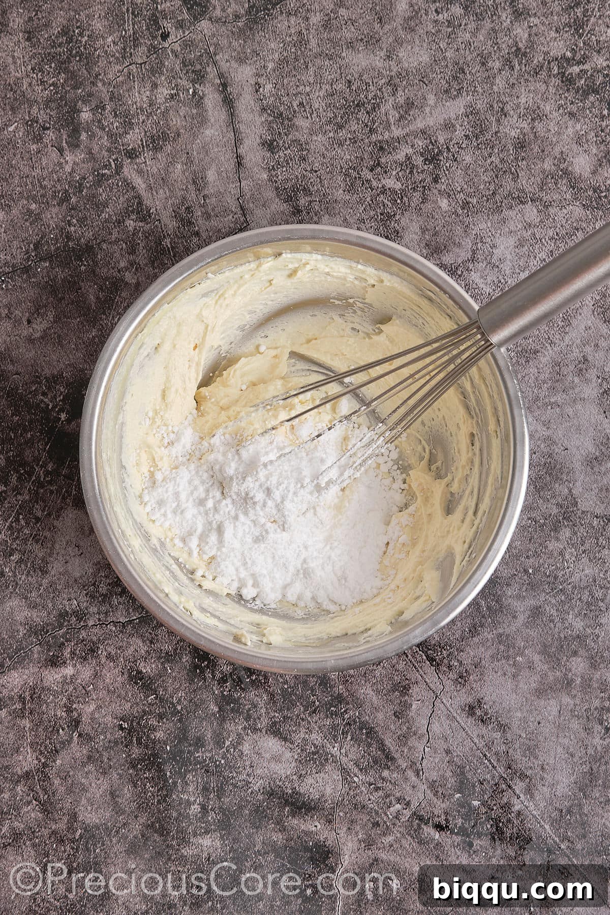 Powdered sugar being added to the cream cheese and butter mixture, being mixed until creamy.
