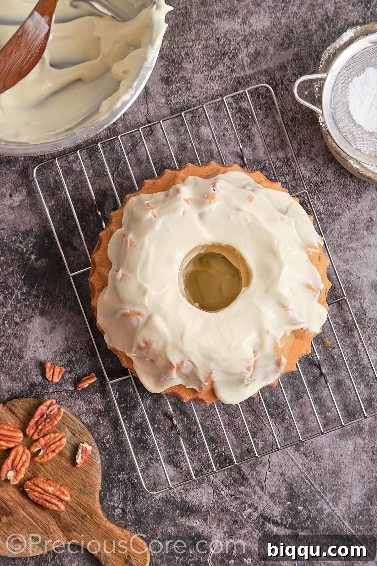 Cream cheese frosting being spread smoothly over the top of the cooled Butter Pecan Pound Cake.