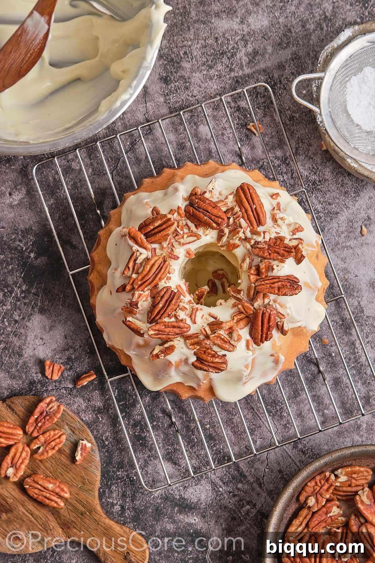 The frosted Butter Pecan Pound Cake being garnished with additional whole pecan nuts for decoration.