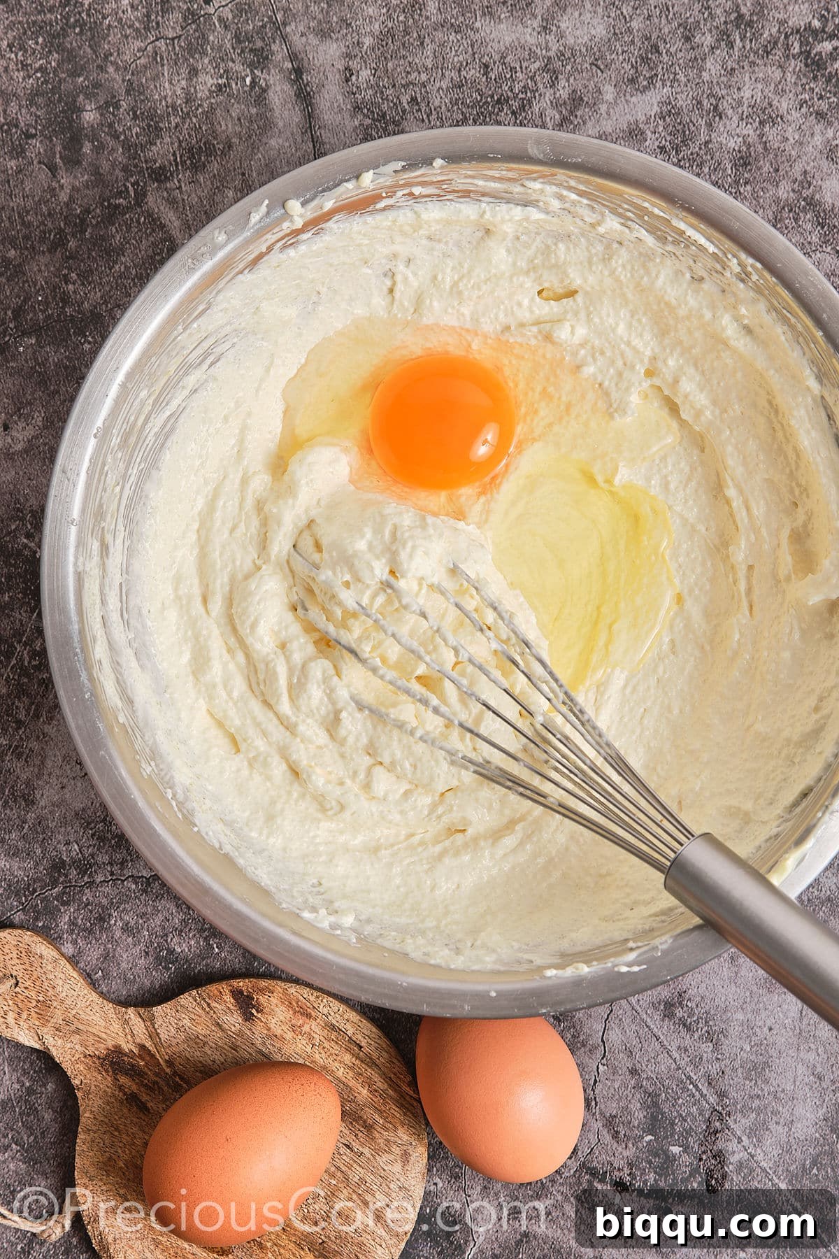 An egg being added to the creamed butter and sugar mixture in a mixing bowl, ready to be incorporated.