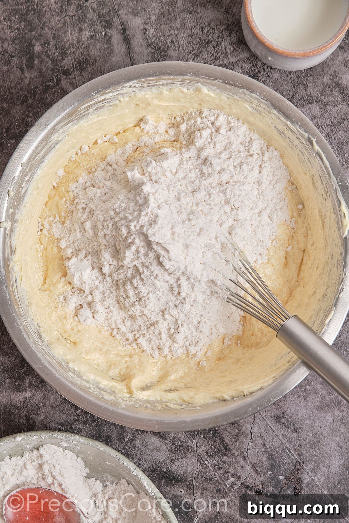 Dry flour mixture being gradually added to the wet batter in a large bowl, being gently mixed.