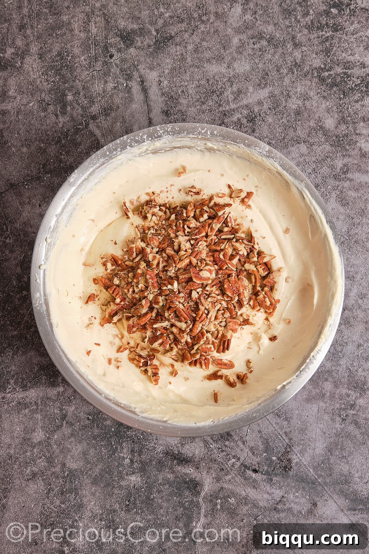 Chopped pecan nuts being folded into the cake batter with a spatula until evenly distributed.
