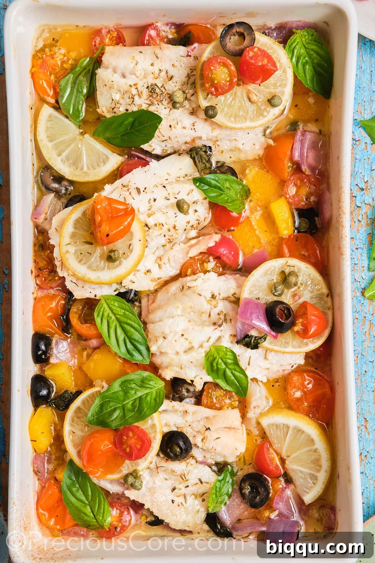 Baking dish with freshly baked Mediterranean fish and vegetables, garnished with fresh herbs and lemon slices.