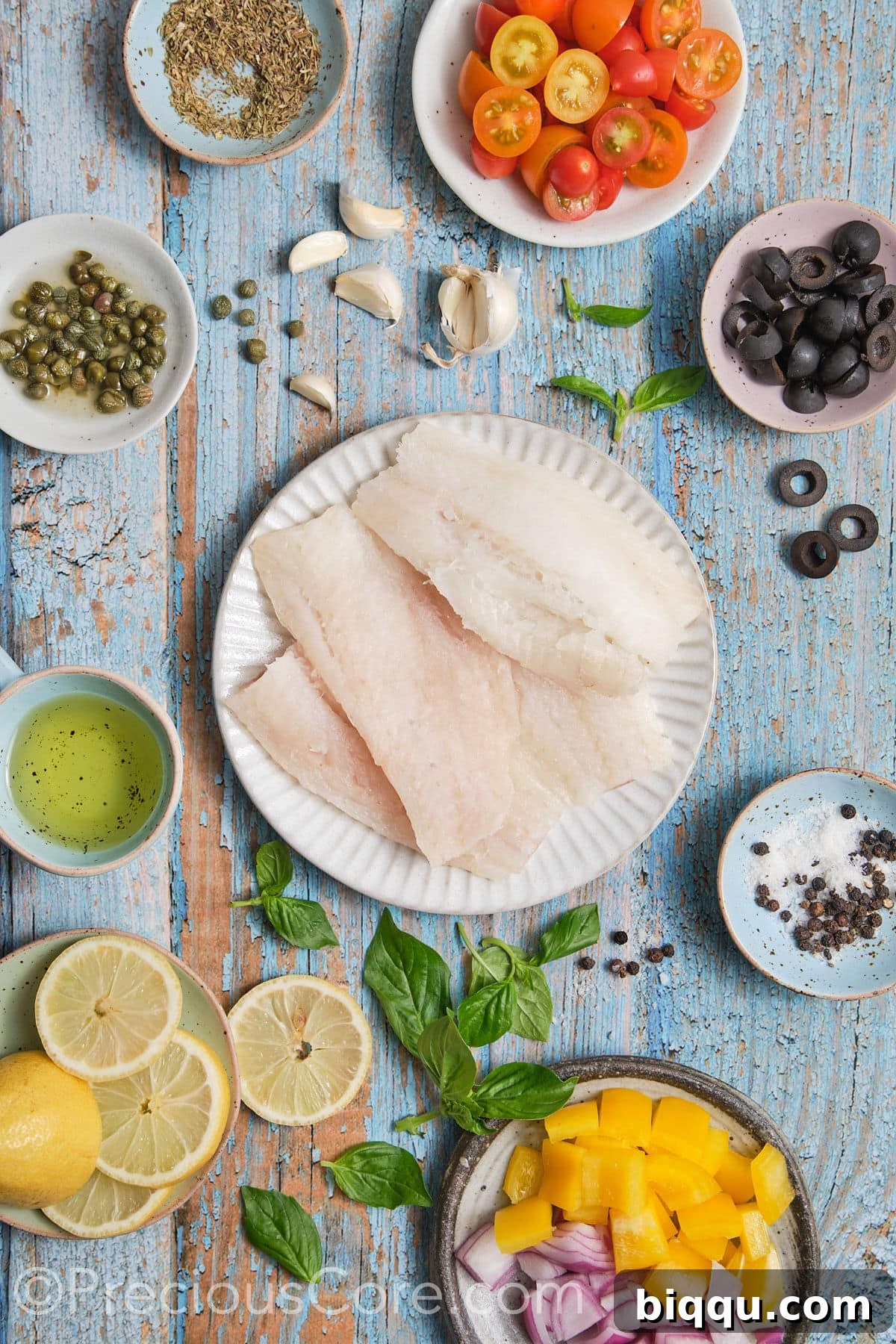 A colorful array of fresh ingredients for Mediterranean baked fish, including cod fillets, cherry tomatoes, olives, lemon, garlic, and herbs.