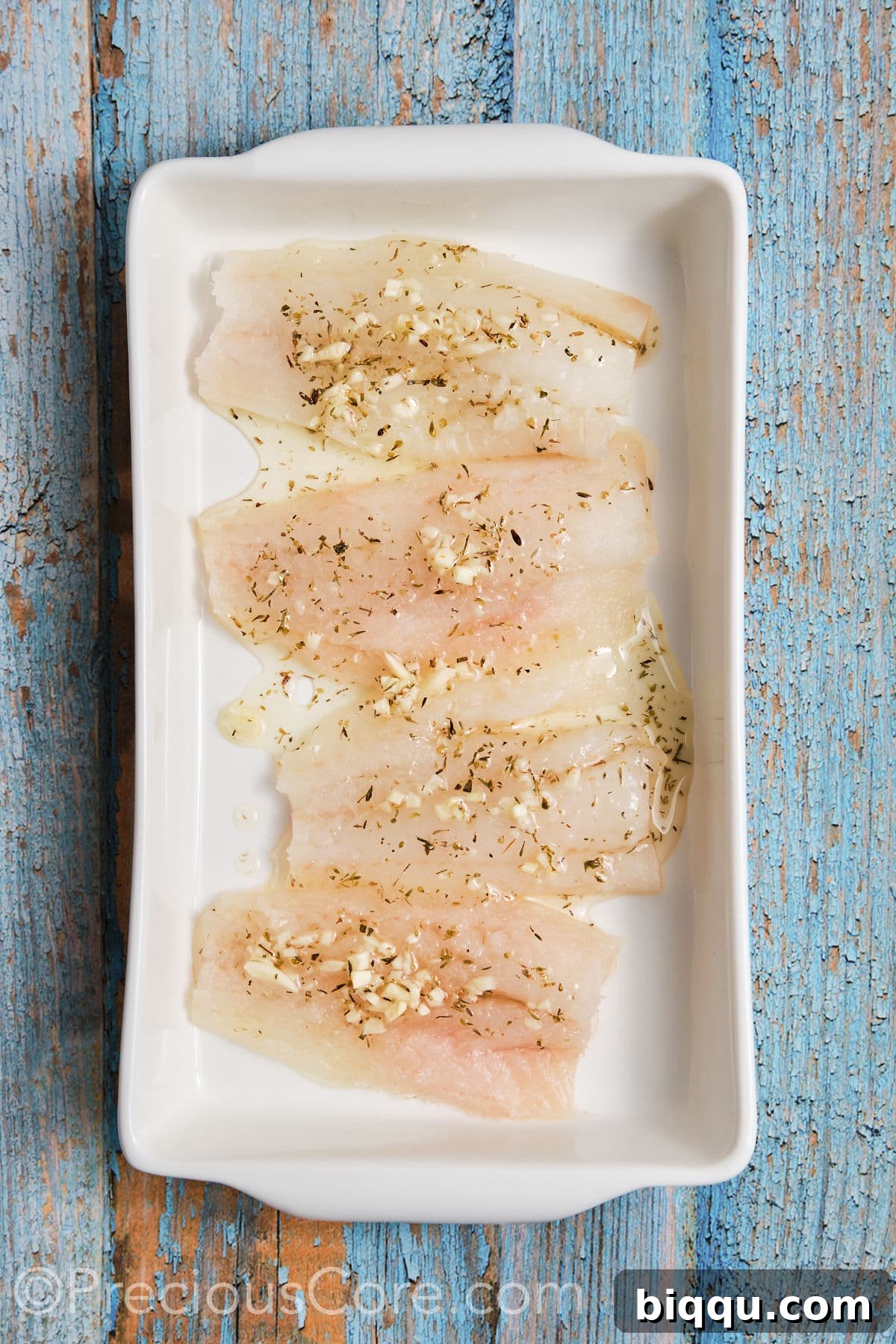 Cod fillets neatly arranged in a shallow pan, thoroughly coated with the Mediterranean marinade.