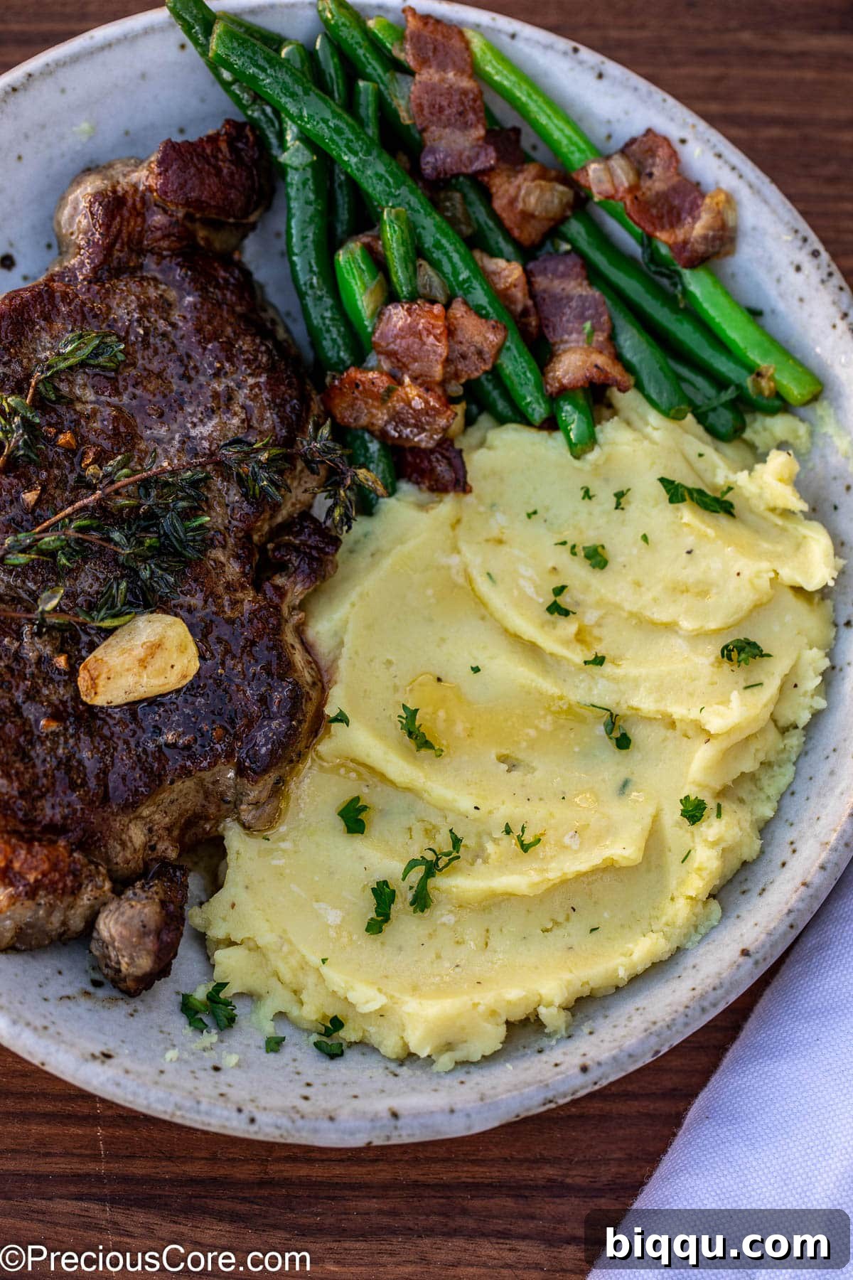 A complete meal featuring a juicy steak, crisp bacon green beans, and a generous serving of mashed white sweet potatoes.