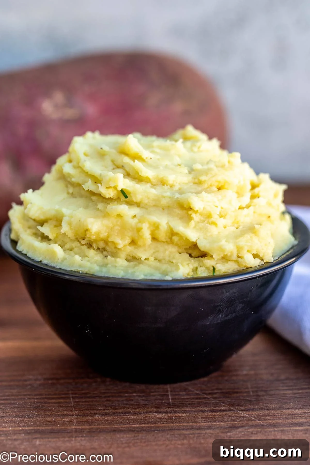 Close-up of mashed white sweet potatoes in a rustic black bowl, garnished with fresh chives.