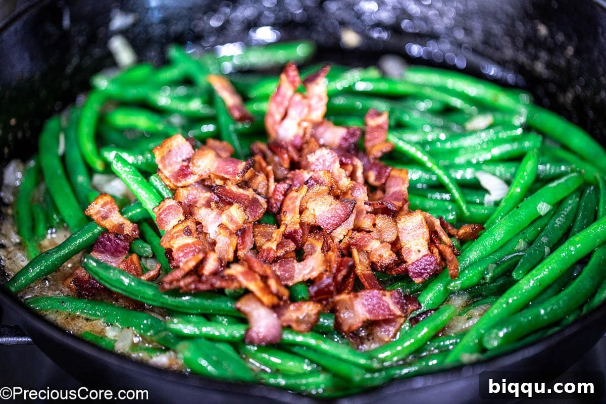 Crispy bacon over green beans in skillet.