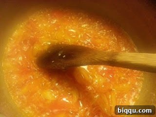 Chopped tomatoes frying in a pot, reducing and deepening in color, with oil beginning to separate from the sauce.