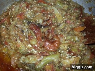A simmering stew base with added ground crayfish, dried fish, seasonings, and peppers, creating a rich aromatic blend.