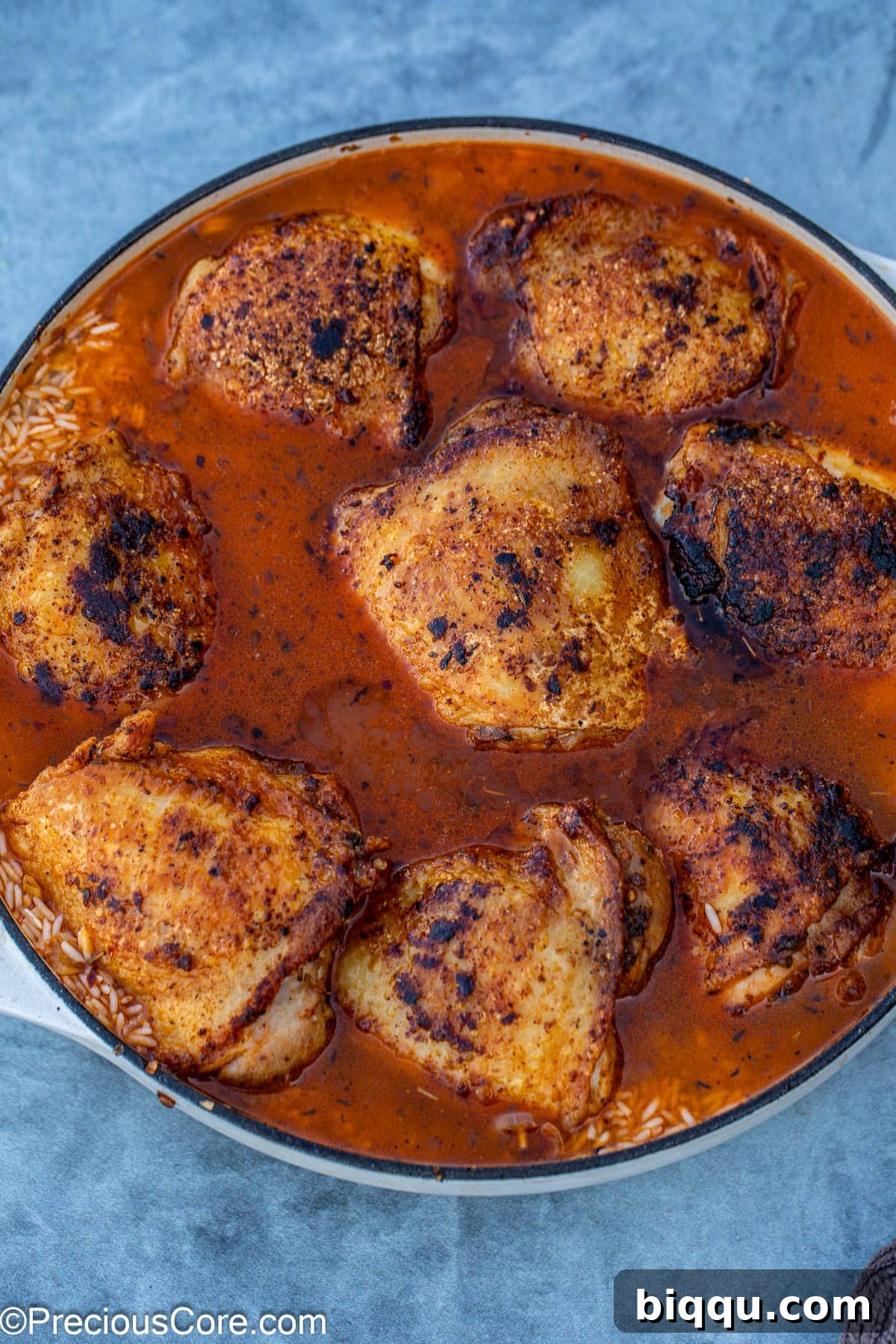 Seared chicken thighs are carefully placed back into the pot, nestled on top of the rice and broth.