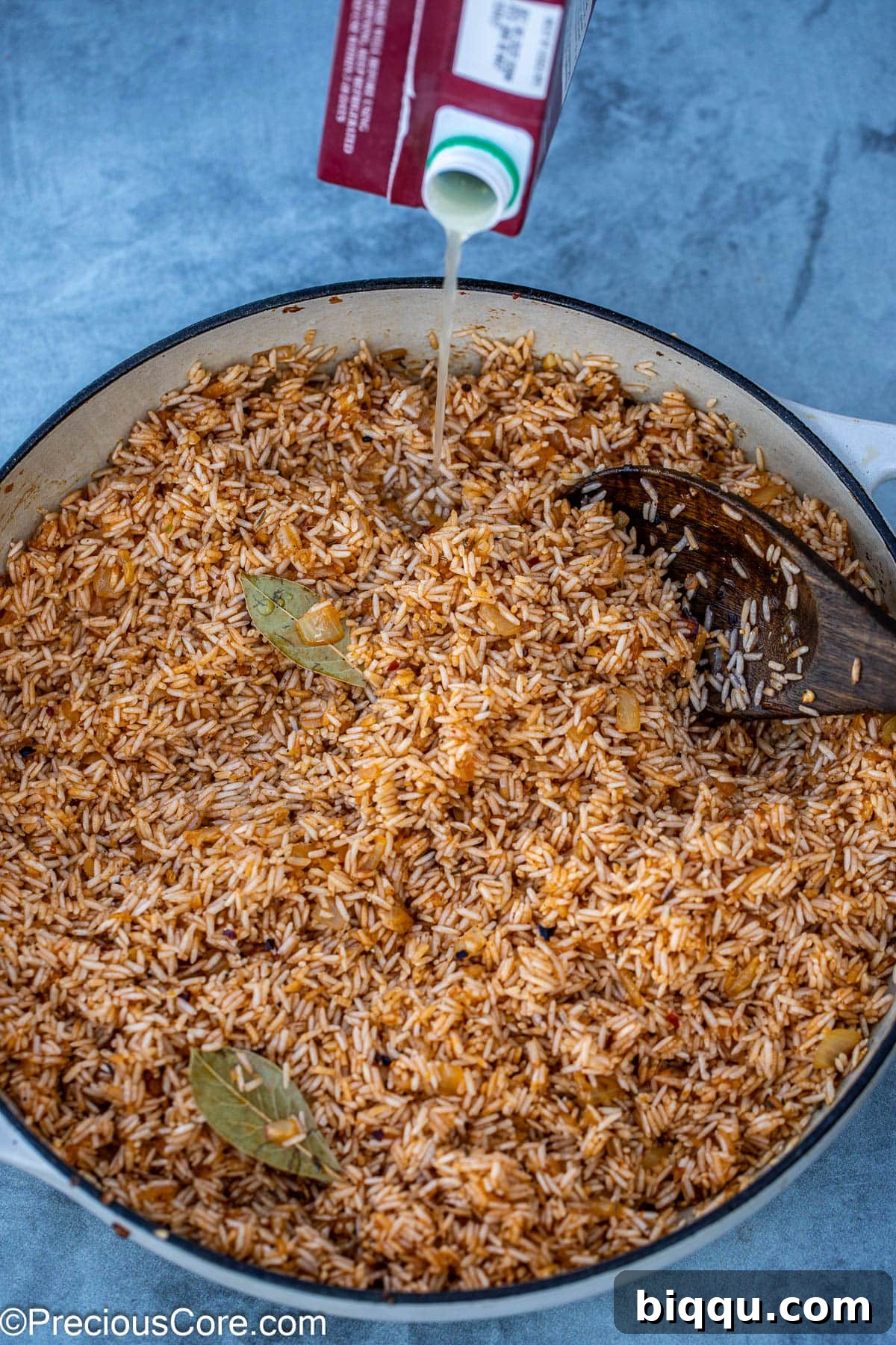 Pouring chicken broth over the rice and seasonings in the pot, preparing for simmering.
