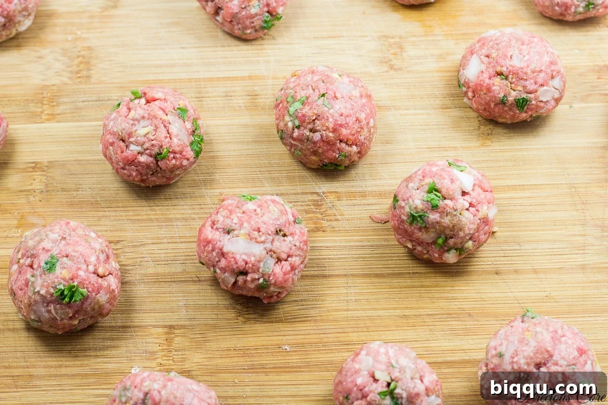 Raw meatballs neatly arranged on a wooden cutting board.
