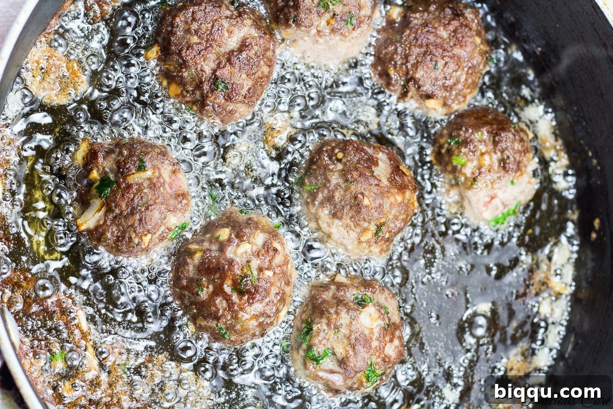 Meatballs frying in a hot pan, turning golden brown.