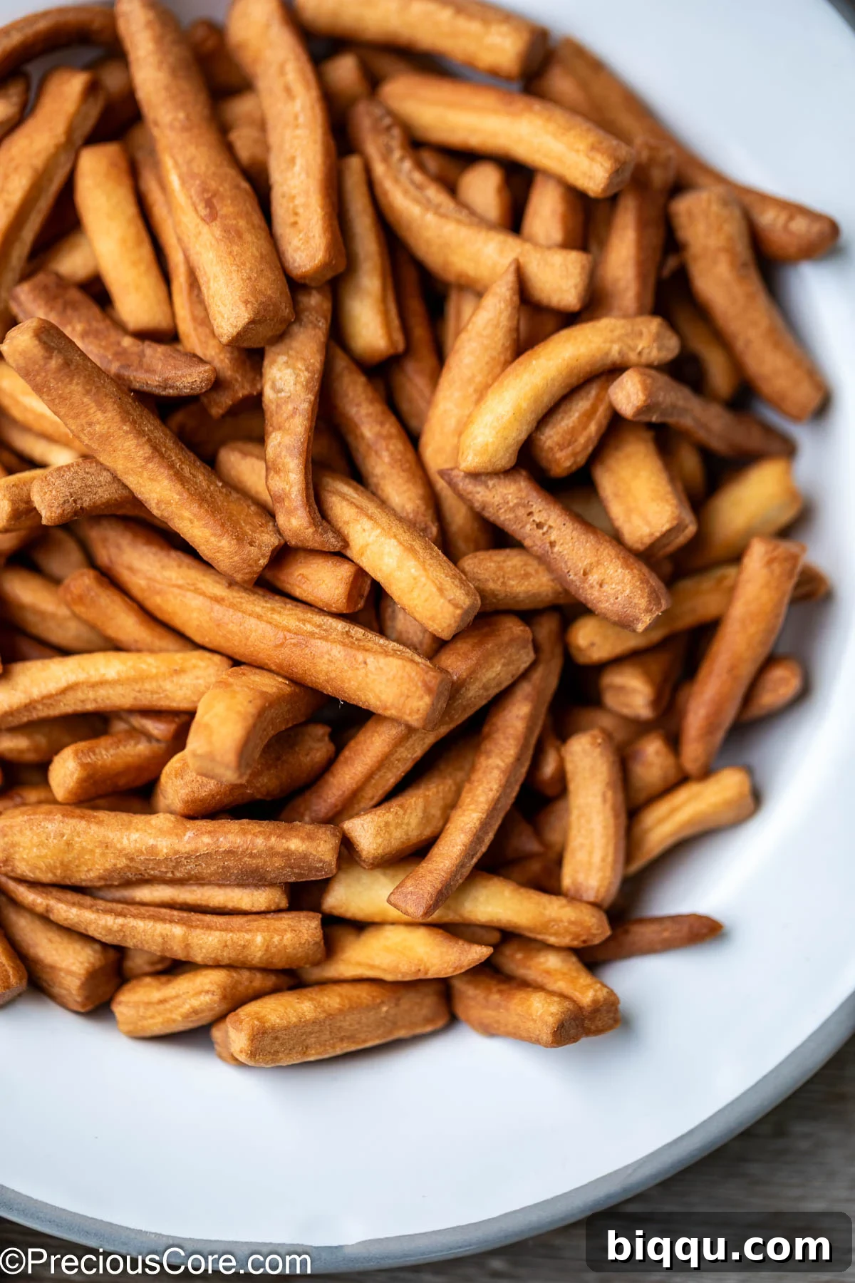 A close-up of golden Chin Chin squares and strips artfully arranged on a pristine white plate, highlighting their appetizing texture and appealing color for a delicious snack.