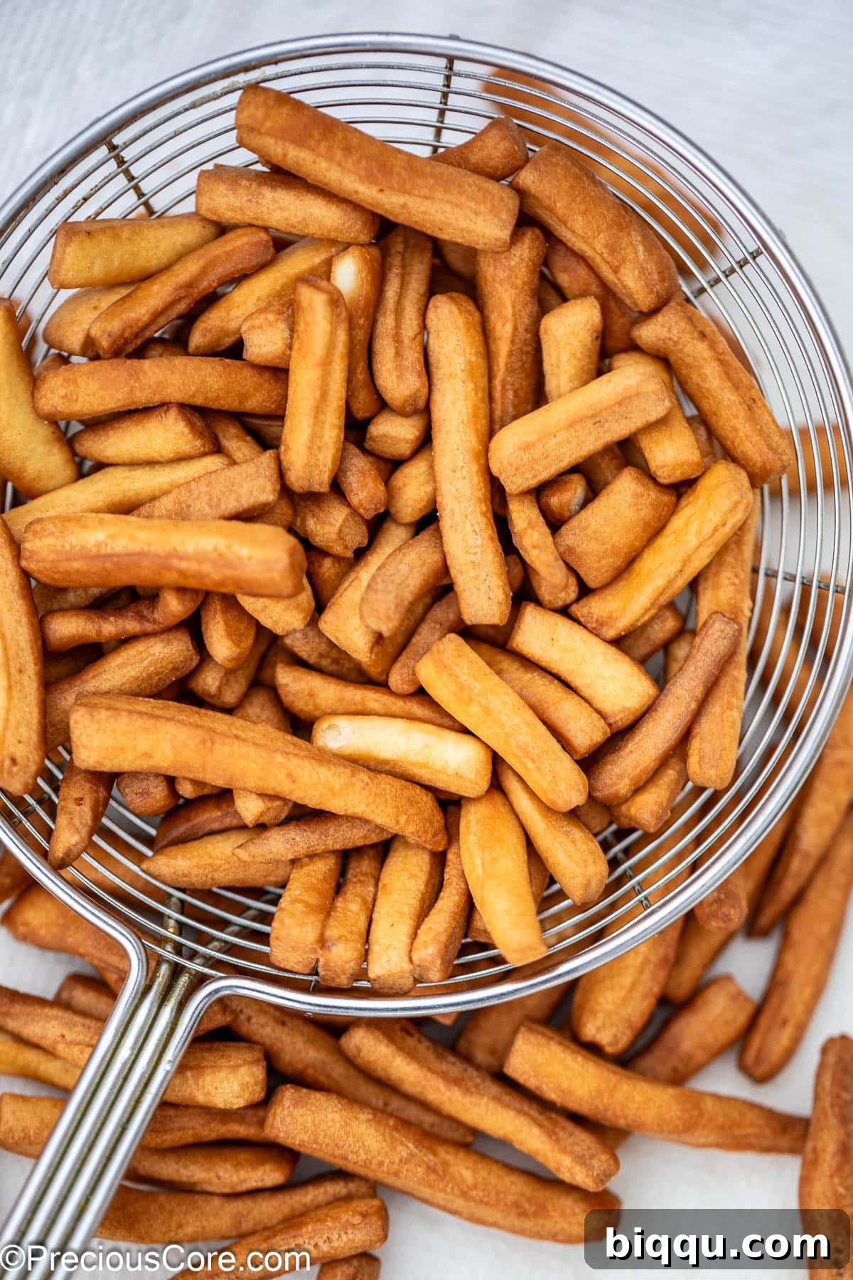 Crunchy Chin Chin pieces being lifted out of hot oil with a slotted frying spoon, showing their golden brown texture and the remaining hot oil in the pot.