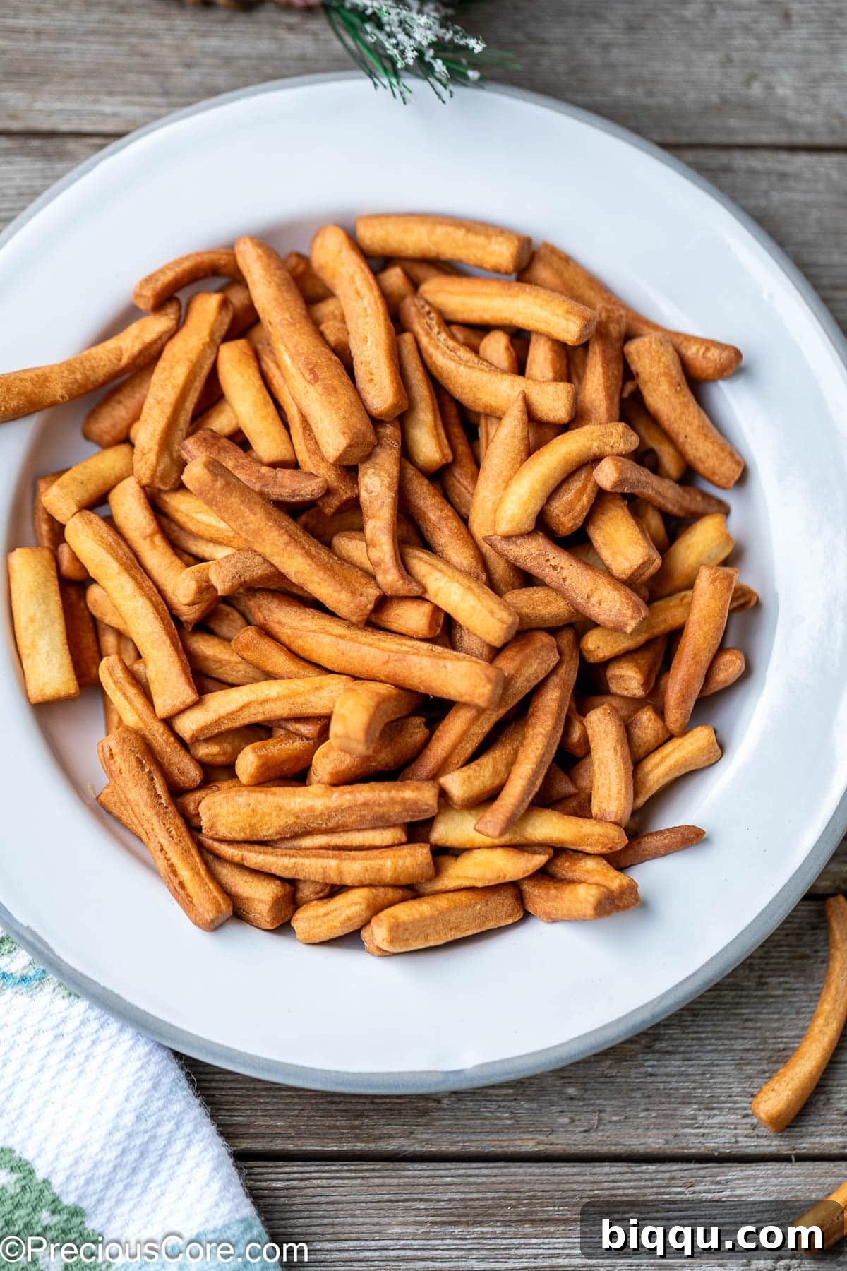 A close-up shot of freshly fried Chin Chin, featuring various shapes including squares and strips, piled high on a white plate, ready for tasting.