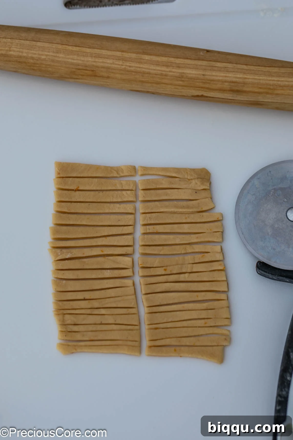 A sheet of Chin Chin dough neatly cut into uniform strips using a pizza cutter, meticulously prepared and ready for frying.