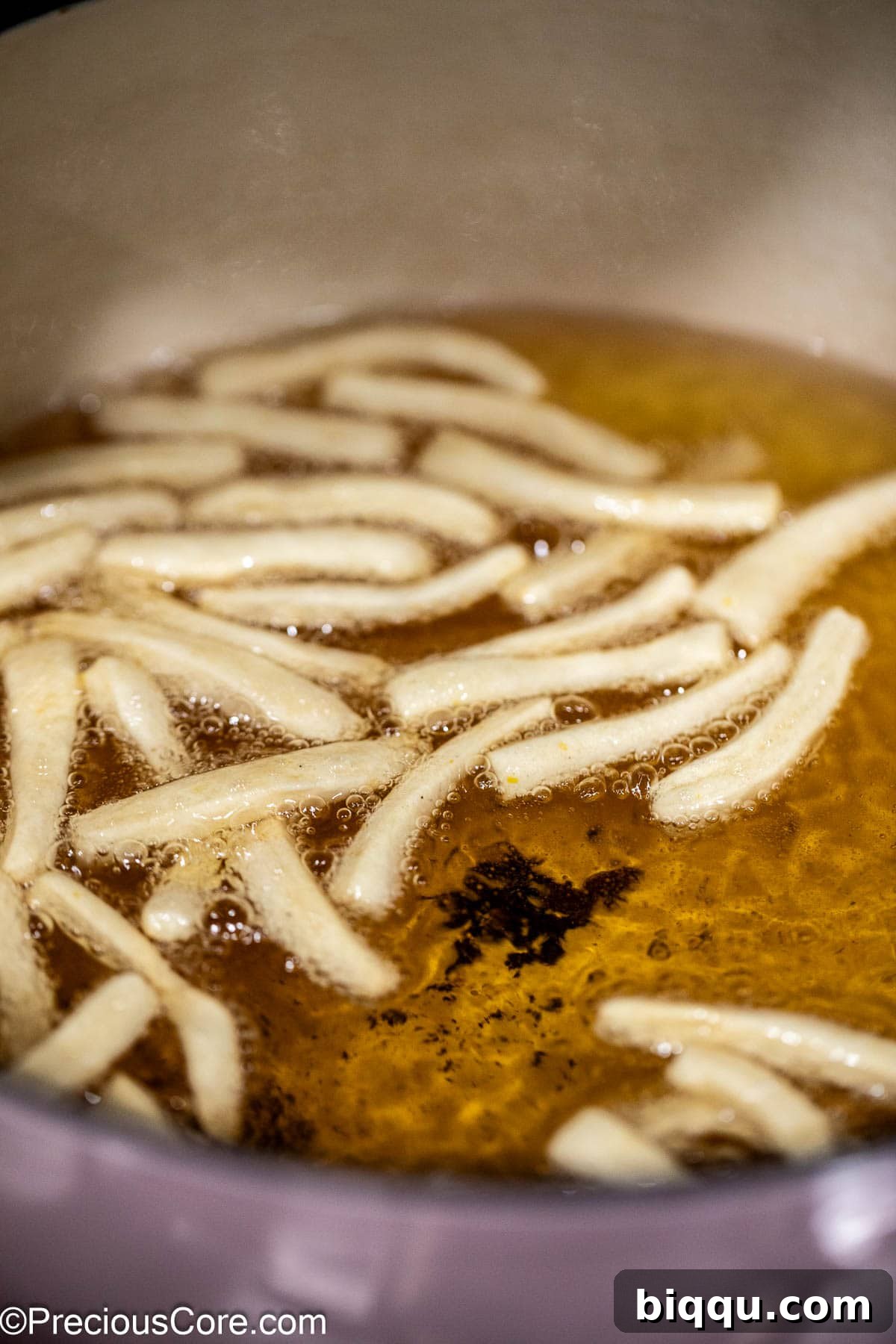 Chin Chin dough strips actively frying in hot oil, bubbling vigorously and beginning to achieve a golden hue.