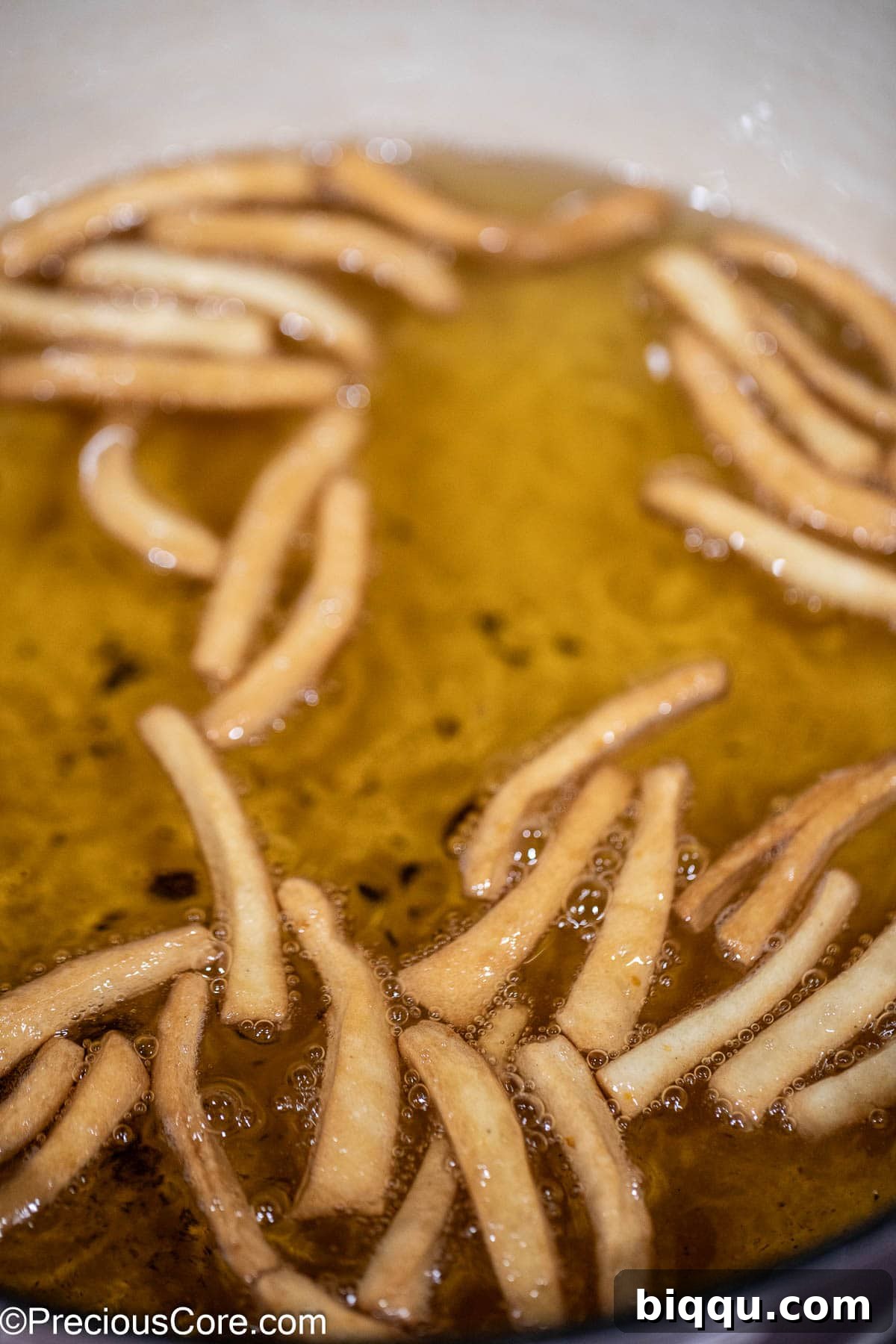 Perfectly golden brown Chin Chin pieces floating in hot oil, almost completely cooked and ready to be removed.