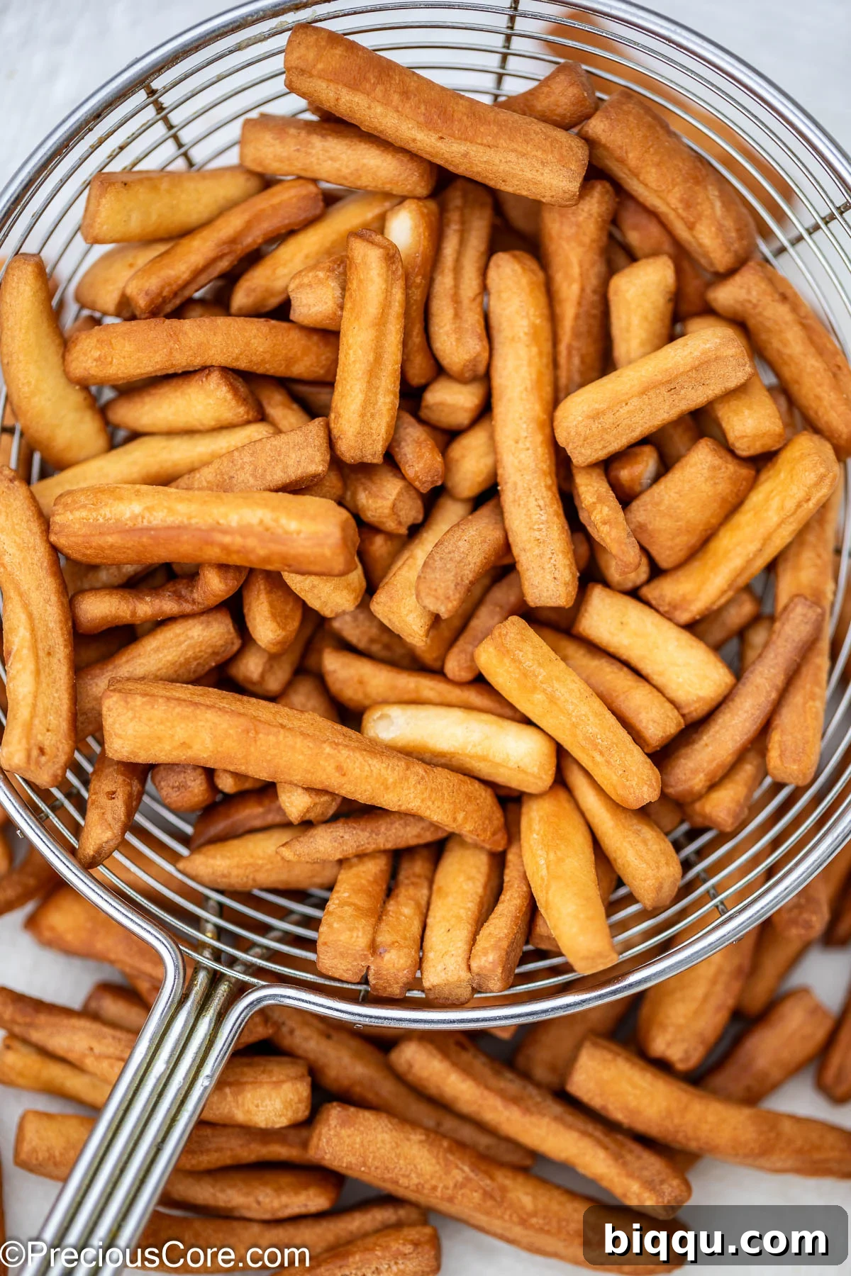 A slotted frying spoon filled to the brim with perfectly golden brown, crunchy Chin Chin pieces, glistening slightly and just removed from the oil.