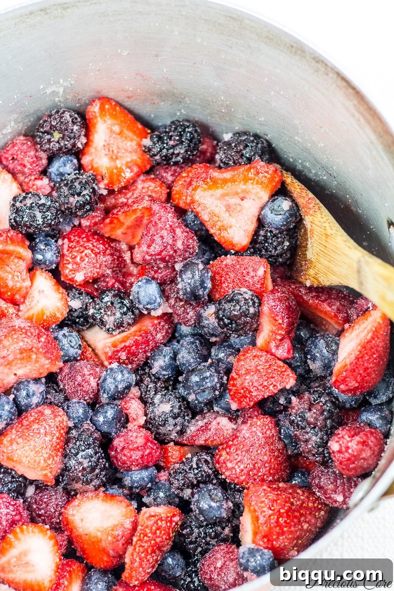 Fresh berries, sugar, and lemon juice macerating in a large pot, ready for cooking.