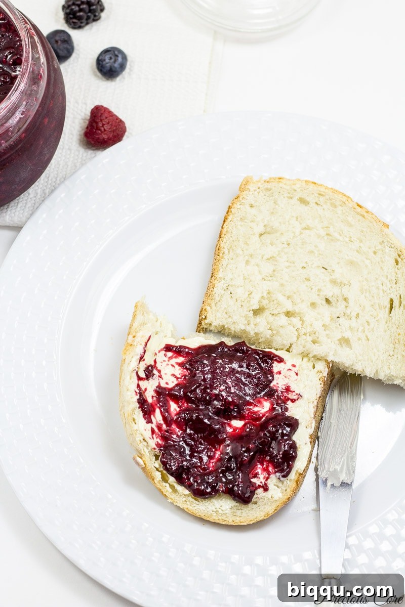 A hand scooping a spoonful of delicious mixed berry jam from a jar, ready to be enjoyed.