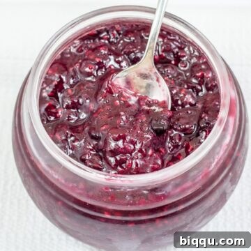 A spoon nestled inside a jar of freshly made mixed berry jam, ready to be served.