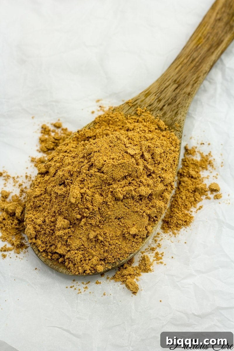A generous scoop of golden-brown homemade suya spice rests on a rustic wooden spoon, hinting at the rich flavors within.