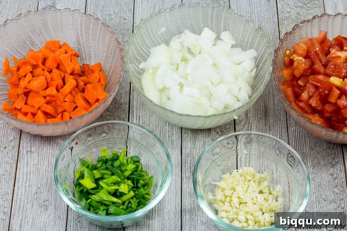 Neatly chopped ingredients for Cameroonian white bean stew including tomatoes, onions, and carrots