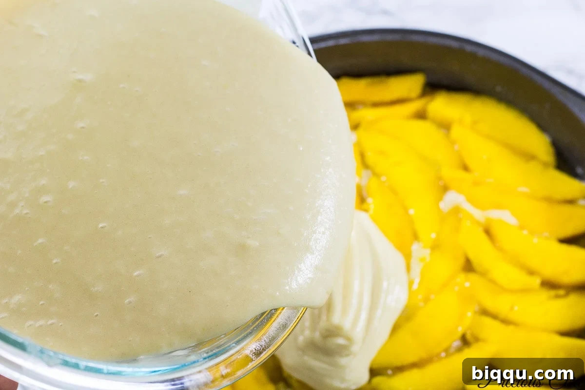 Cake batter being poured over arranged mango slices