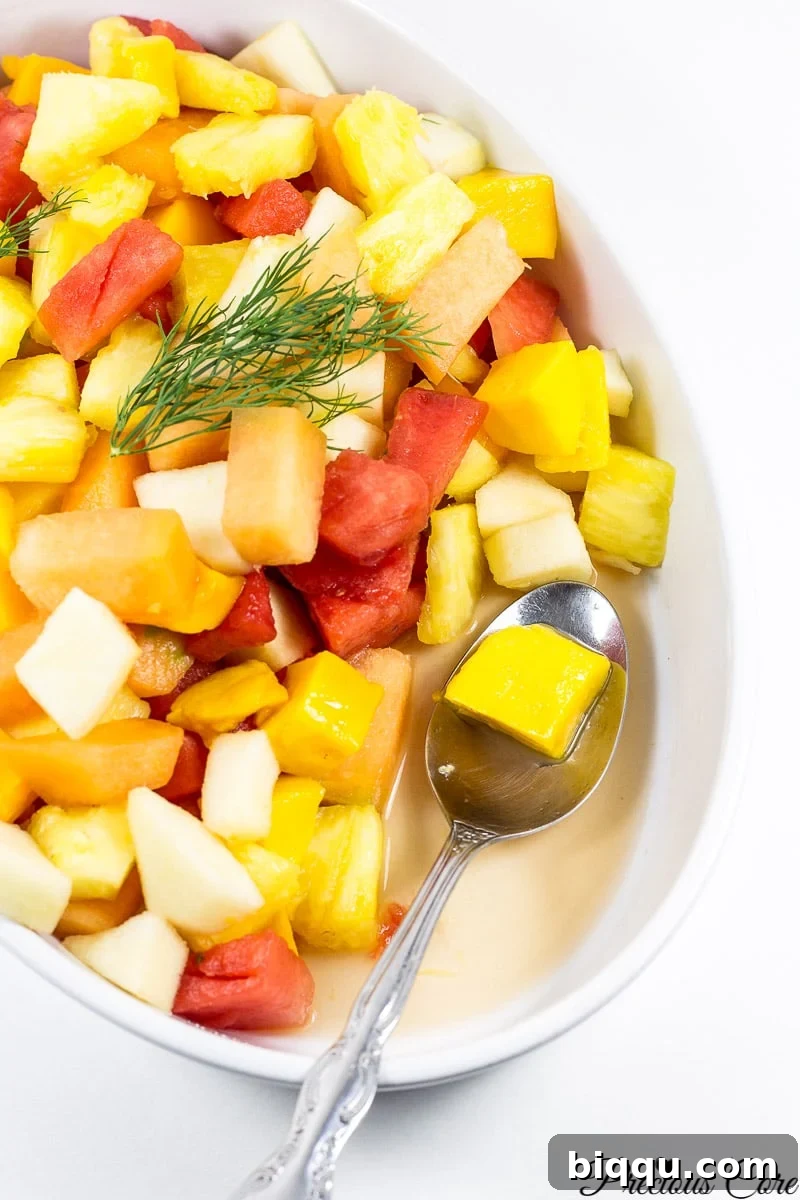 A spoon delicately scooping a portion of the colorful Cameroonian fruit salad from a large bowl, highlighting its refreshing appeal and ready-to-eat nature.
