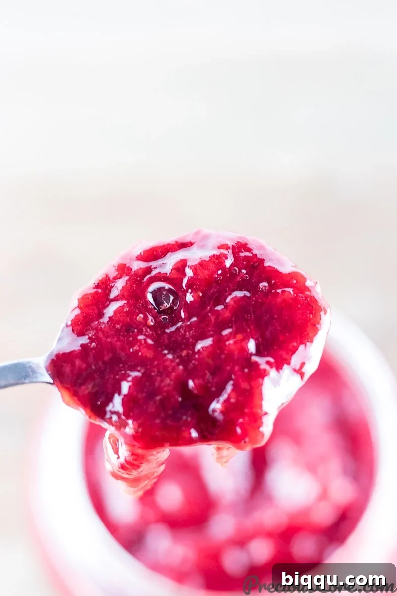 Spoon scooping healthy strawberry jam from a glass jar, showcasing its beautiful texture.