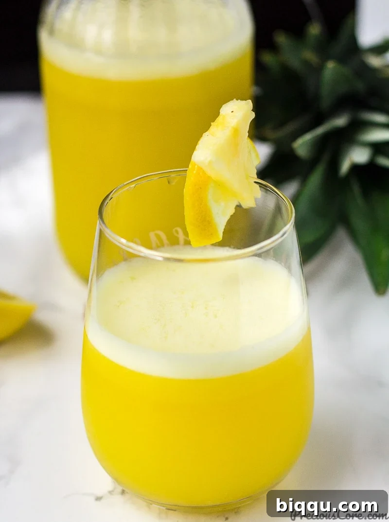 Tropical Ginger Kick 2 Refreshing Pineapple Ginger Juice in a glass, garnished with a pineapple wedge and ginger slice.