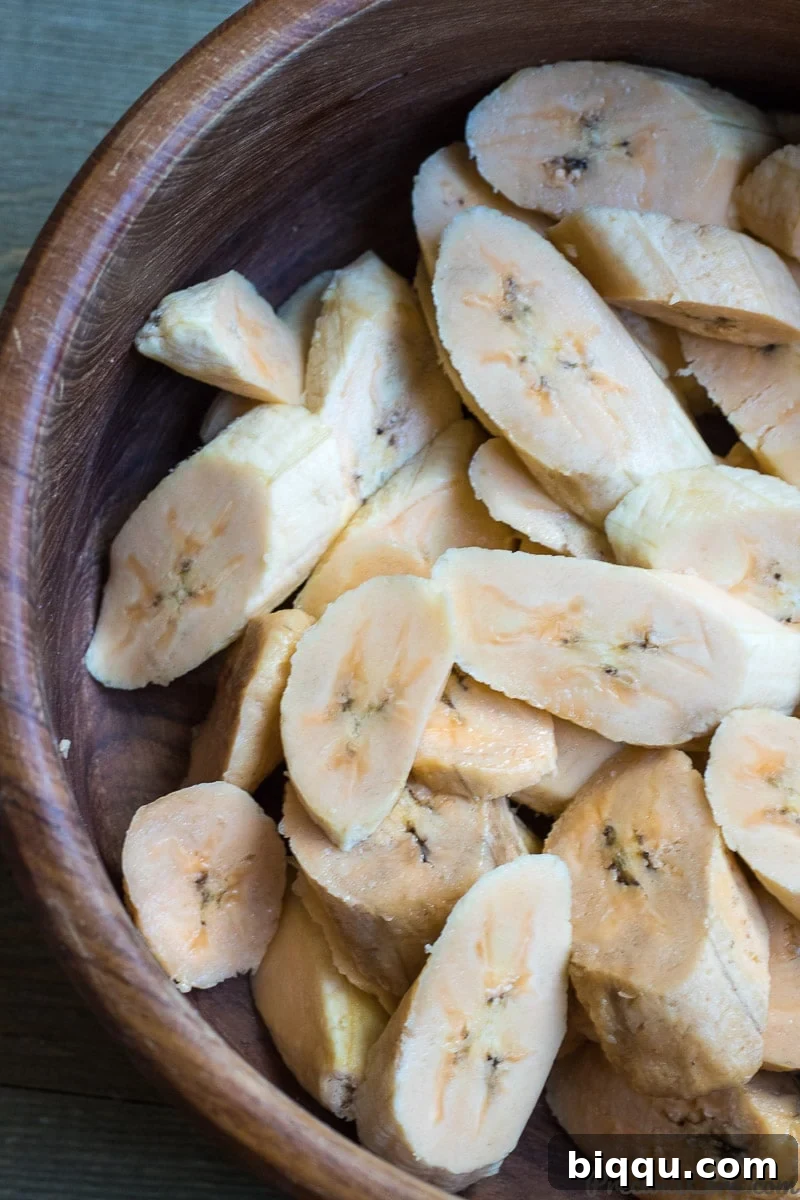 Freshly sliced sweet plantains, cut diagonally, gathered in a natural wooden bowl.