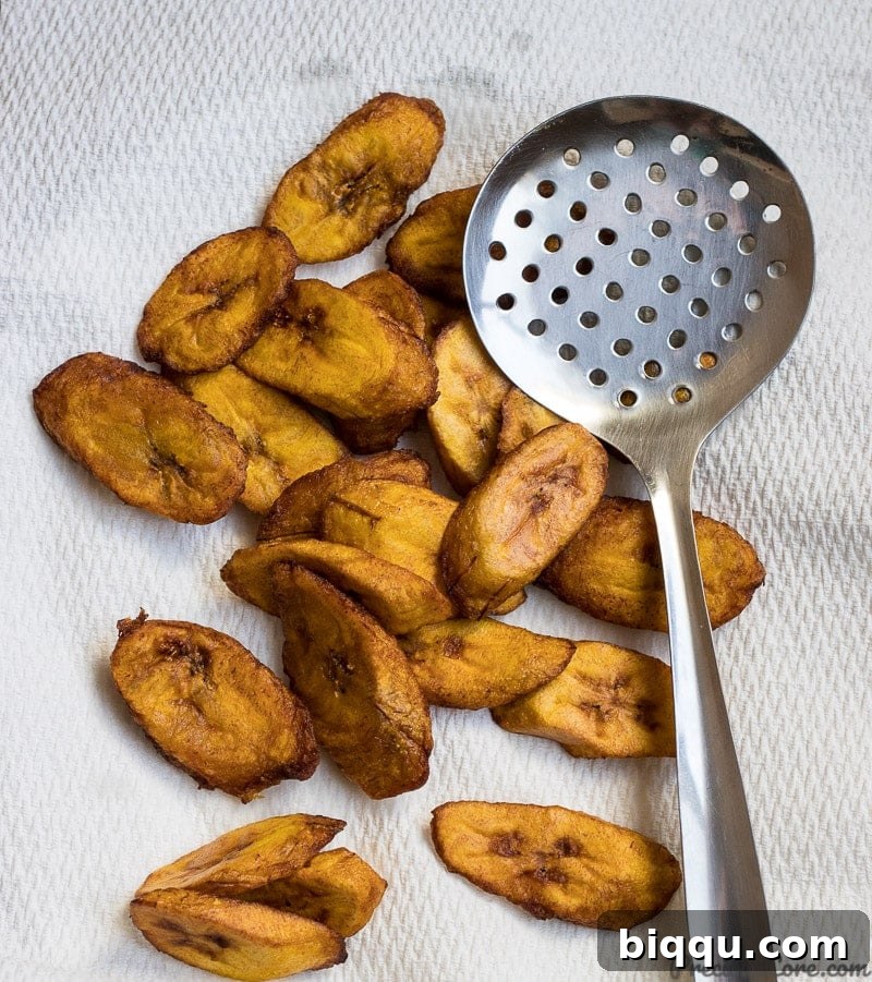 Freshly fried, golden brown sweet plantains resting on paper towels to drain excess oil.