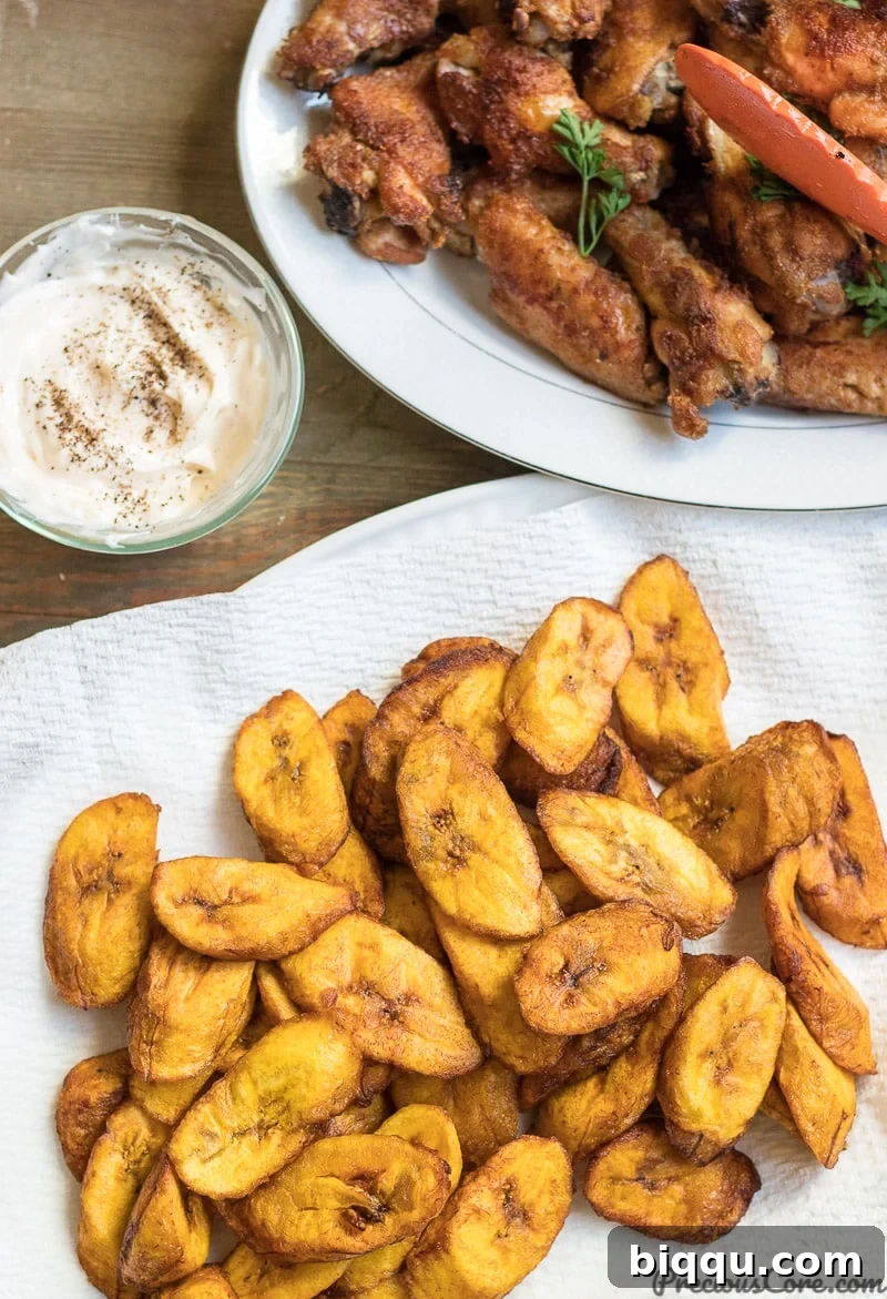 A plate of golden fried plantains served alongside savory grilled chicken wings, showcasing a perfect meal pairing.