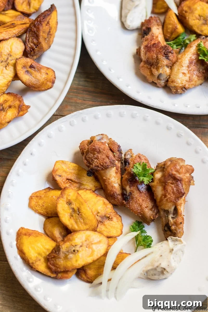 Close-up of sweet fried plantains on a white plate, served with perfectly oven-grilled chicken wings in the background.
