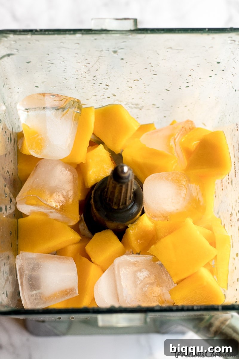 Chopped mangoes in a blender with water and ice for mango juice