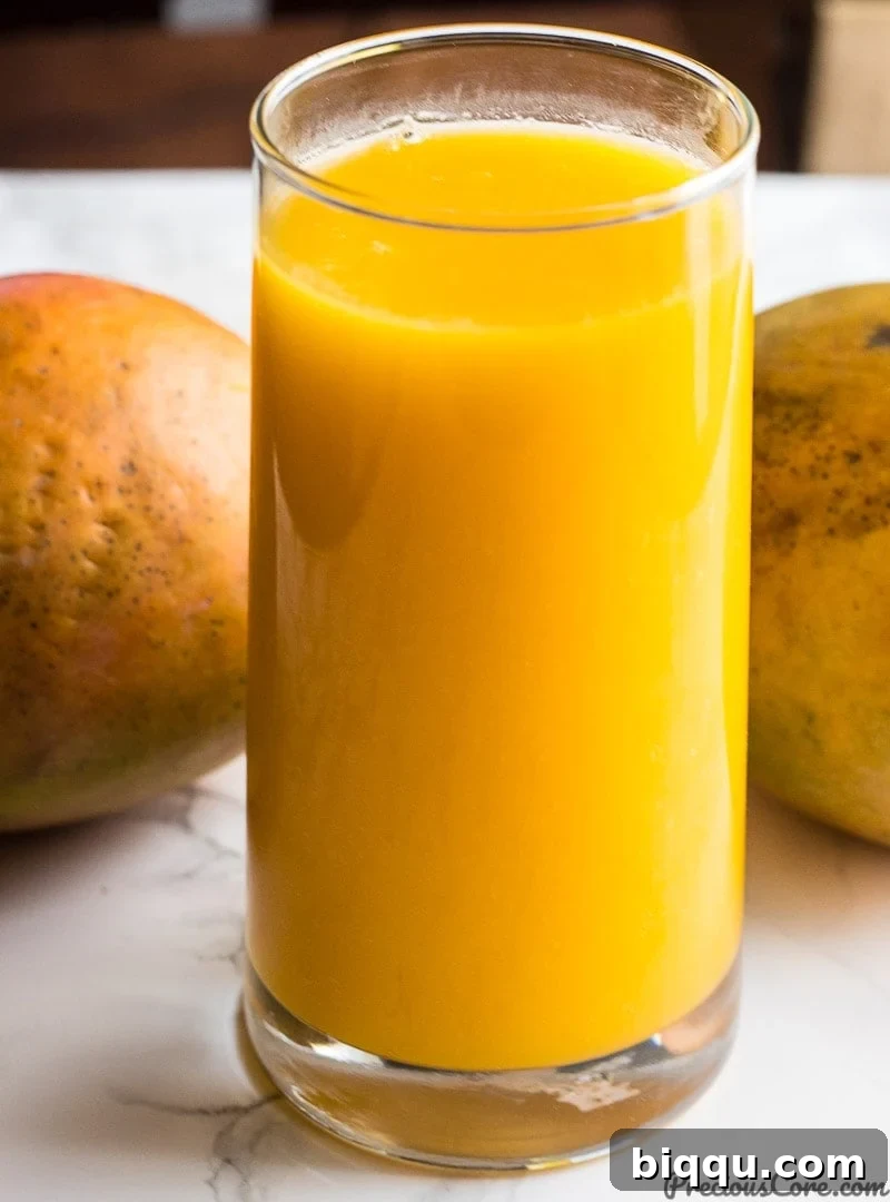 Mango Juice Recipe - A tall glass of creamy, golden mango juice, adorned with fresh mango slices and a small umbrella, evoking a tropical paradise.