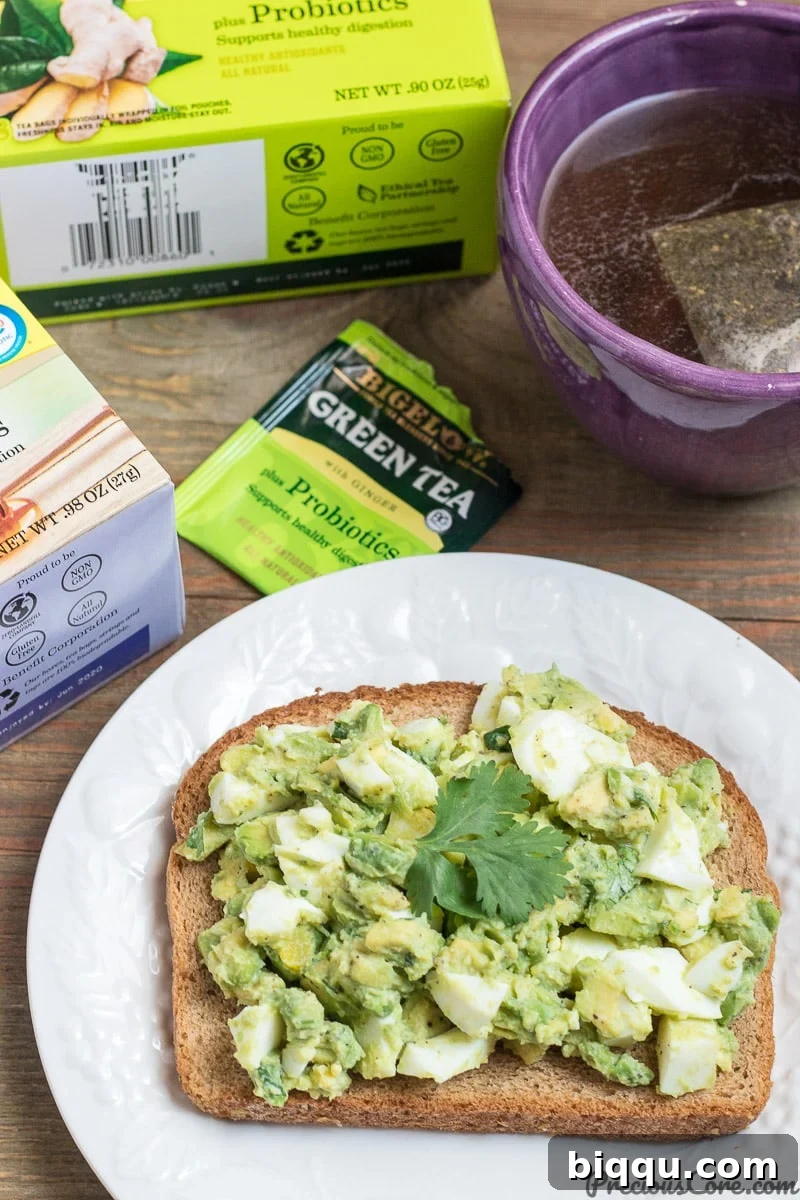 A breakfast spread featuring avocado egg salad on toast with two cups of Bigelow probiotic teas.
