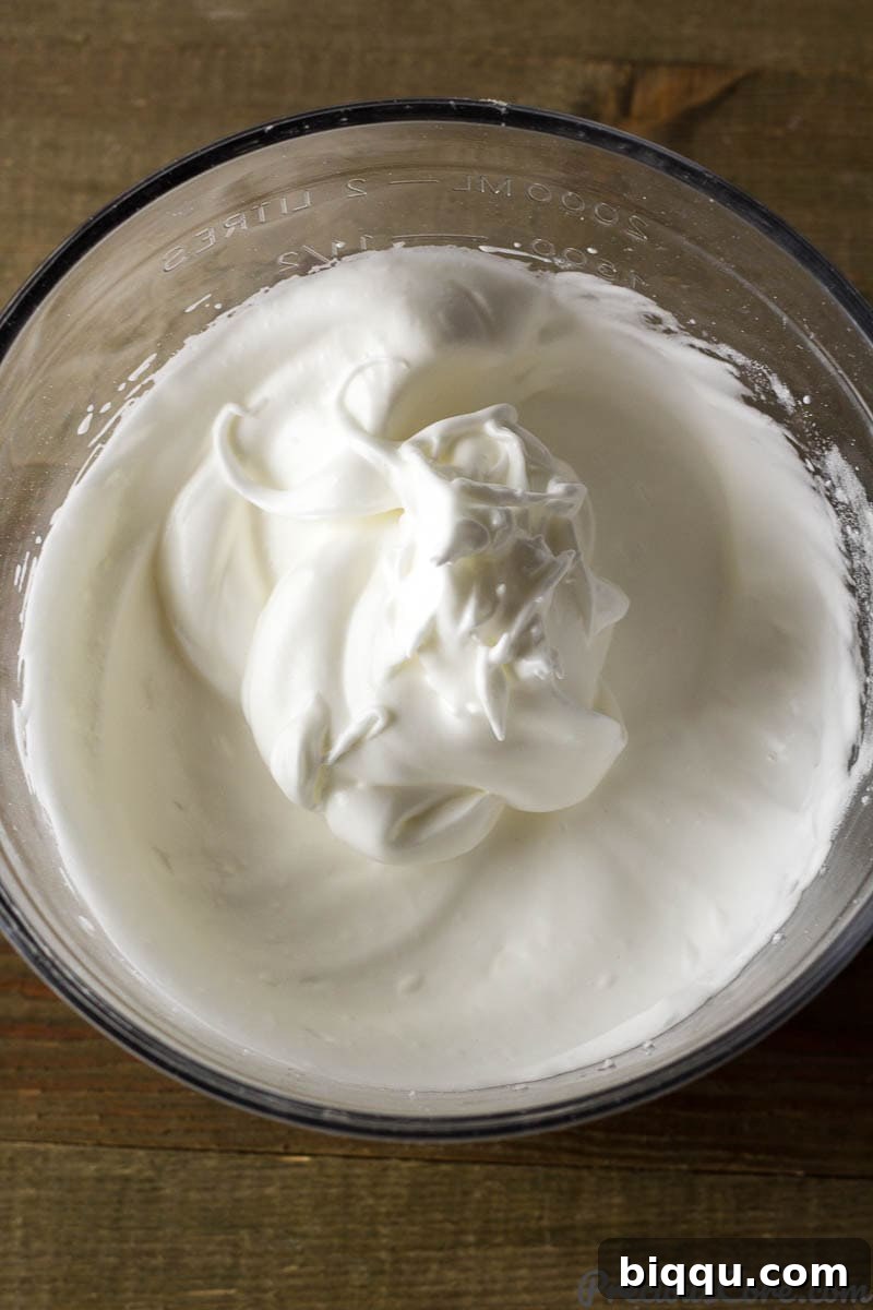 Fluffy Vanilla Sponge Cake 4 A glass bowl filled with perfectly whipped egg whites, forming stiff peaks.