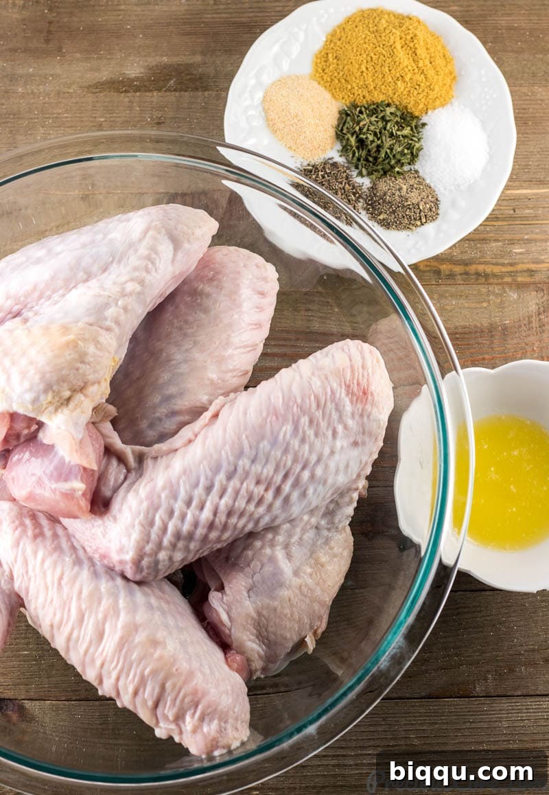 Fresh turkey wings in a bowl, a selection of vibrant spices and herbs on a plate, and a small bowl of golden melted butter.