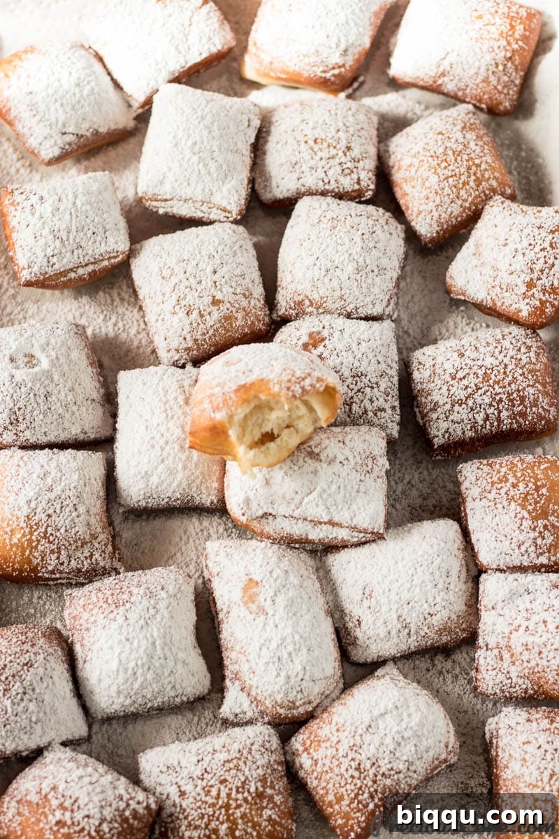 A tray filled with freshly made New Orleans beignets, one with a bite taken out, dusted generously with powdered sugar.
