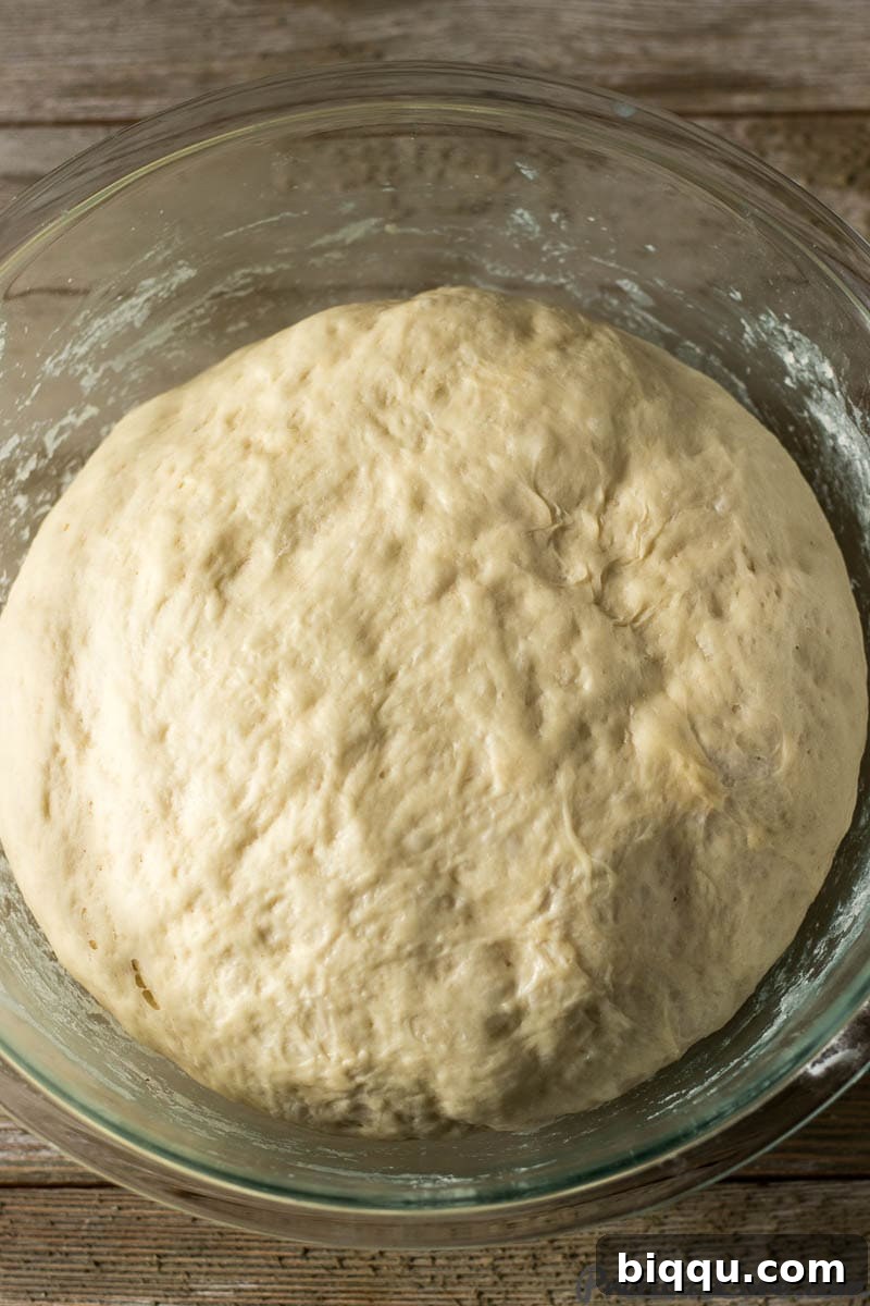 Close-up shot of light, airy beignet dough after rising, contained within a clear glass mixing bowl.
