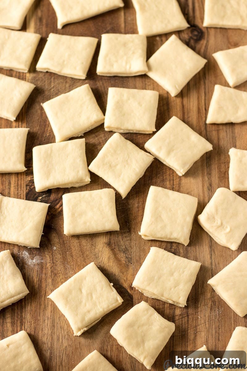 Several neatly cut squares of beignet dough arranged on a light wooden surface, awaiting their transformation through frying.